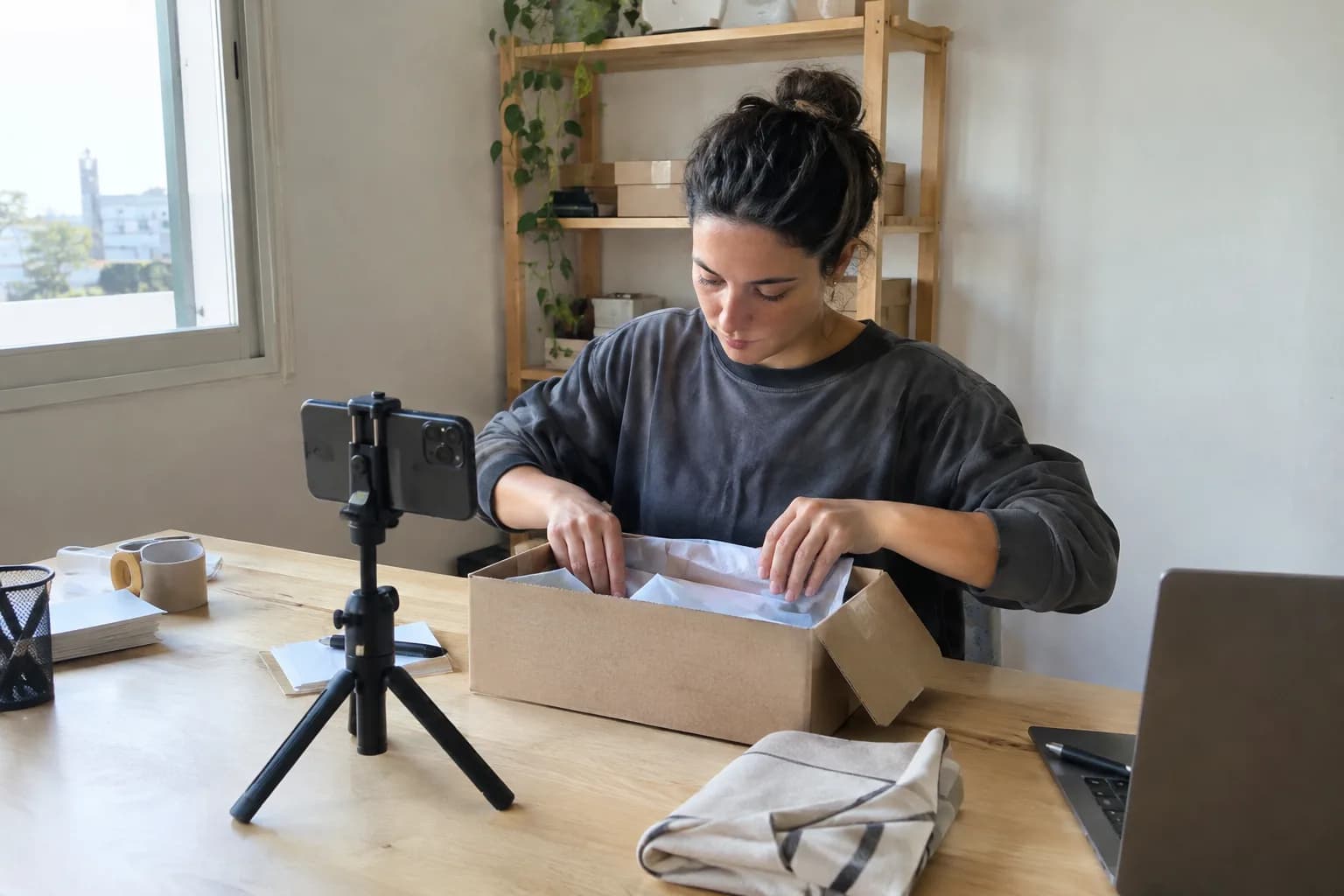 An online store owner packs an order while filming a marketing video for her product.